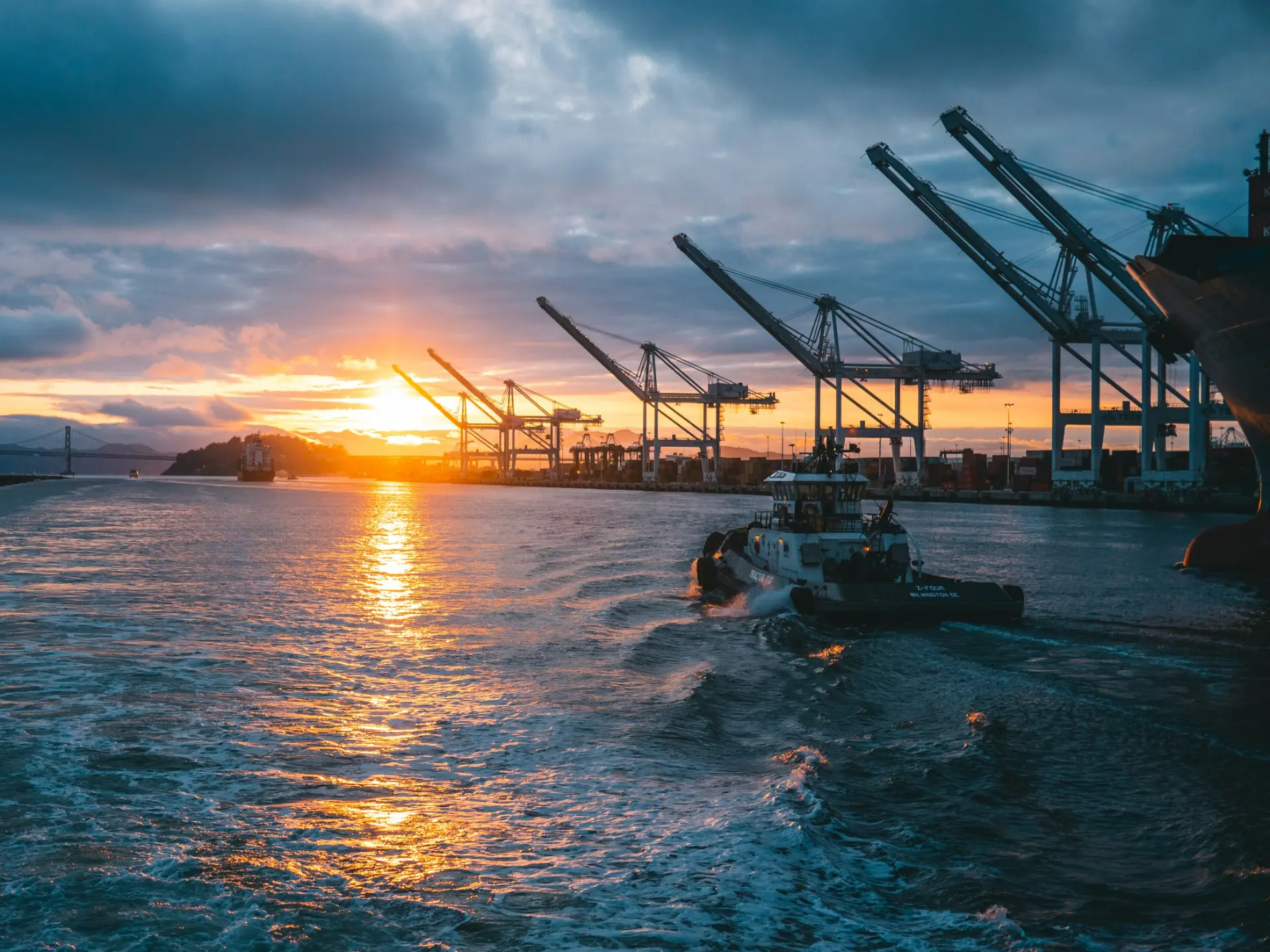 Industrial port at sunset with cranes and a tugboat, an operational technology environment protected by OT cyber security